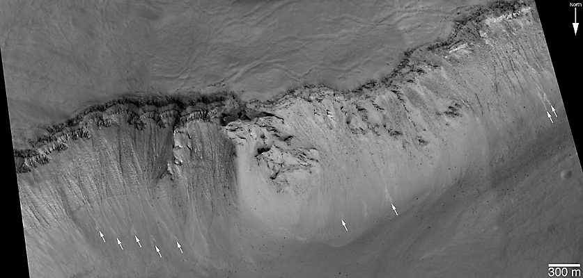 Slope with gullies, boulders, layers, and several light-toned deposits.